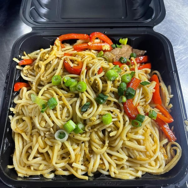 Hibachi Bus Stop hibachi noodles with red peppers, meat, and green onions in a black takeout container.