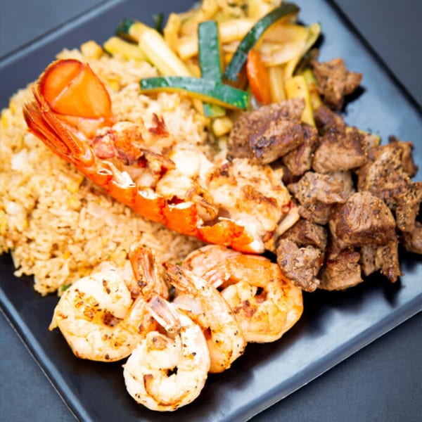 Hibachi Bus Stop's lobster, shrimp, steak, fried rice, and vegetables on a black plate.
