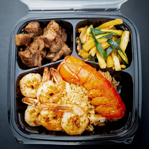 Hibachi Bus Stop hibachi meal with steak, shrimp, lobster, fried rice, and vegetables in a black container.