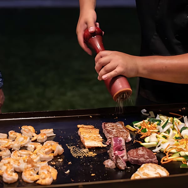 A chef seasons shrimp, steak, and vegetables cooking on a hibachi grill at Hibachi Bus Stop.