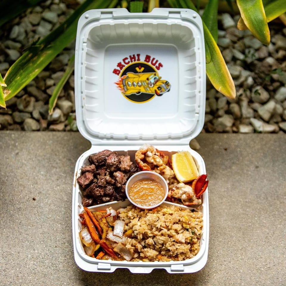 Hibachi Bus Stop takeout box with steak, lobster, fried rice, vegetables, sauce, and lemon.